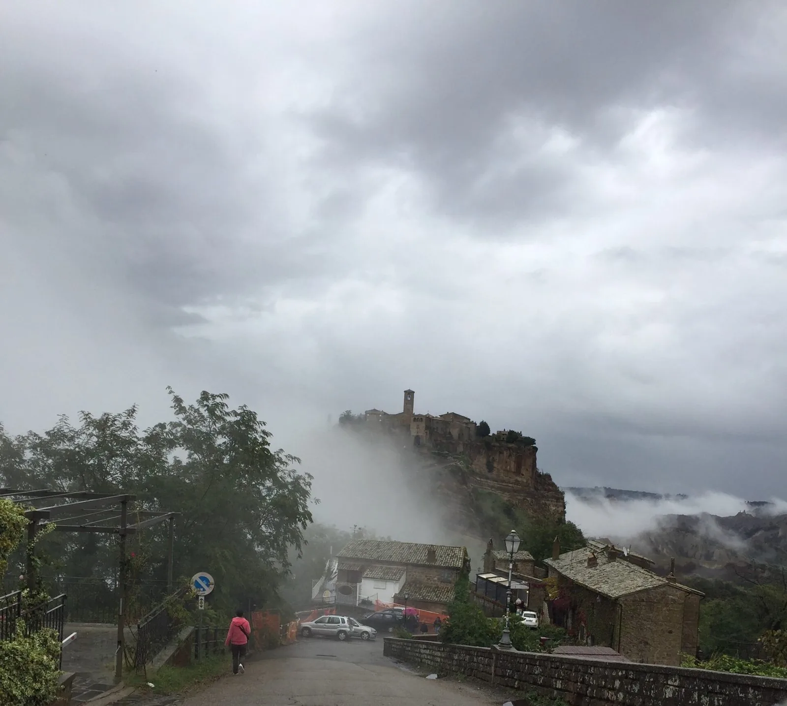 Civita di Bagnoregio avvolta dalla nebbia in una giornata grigia, vista dalla strada che scende verso il ponte